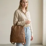 Mochila urbana de diseño versátil, confeccionada en eco-cuero color marrón con acabado texturizado. Presenta un compartimento principal con cierre, bolsillo frontal con logo grabado y correas ajustables.
