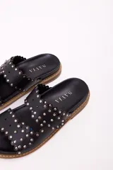 Sandalia tipo mule de mujer, color dorado metalizado, con dos tiras anchas superpuestas con borde festoneado y tachas doradas. La suela es gruesa y de color marrón claro.