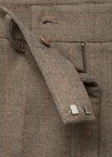 Pantalón de tiro medio color marrón con sutil diseño de raya diplomática, de corte entallado y diseño crop. Cuenta con bolsillos laterales, trabillas y cierre frontal con cremallera, botón y ganchos ocultos.