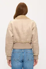 Campera corta tipo aviador en color beige, confeccionada en material con textura gamuzada y forro interno de corderito sintético. Presenta cierre frontal, bolsillos laterales con solapa y puños y ruedo en tejido acanalado.