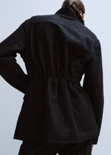 Parka de denim negro de corte largo, con cuello alto, cierre frontal oculto y múltiples bolsillos con solapa en el pecho y los costados. Cuenta con cordón ajustable en la cintura.