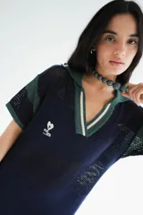 Remerón tejido de punto color azul marino con calados, cuello estilo camisa en verde oscuro con rayas blancas y verdes, y logo bordado en blanco en el pecho.