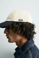Gorra de seis paneles, color beige, con visera azul marino. Presenta bordado frontal con el texto "Genuine Ford Parts" en tonos azul y rojo, y un pequeño parche bordado con el logo de Ford en el lateral.