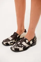 Mocasín de cuero con pelo y estampado de vaca en blanco y negro. Presenta horma cuadrada, diseño enrejillado en la capellada y taco bajo de 4,5 cm.