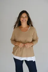 Sweater de punto color camel con diseño de doble capa, escote en V con detalle de vivo plateado y mangas largas. El diseño presenta un bajo asimétrico con una capa inferior blanca visible.