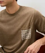 Remera Marfinno de manga corta y cuello redondo, de color tostado, confeccionada en tejido de punto con mezcla de poliéster, elastano y poliamida. Cuenta con un bolsillo frontal aplicado en el pecho con diseño geométrico en color blanco.