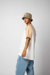 Remera estilo raglán color blanco en el cuerpo, con mangas en tono tostado y ribetes en color verde militar en el cuello y los puños.