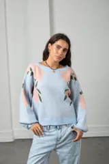 Buzo de punto color celeste con estampado de flores rosadas y hojas verdes. Presenta cuello redondo, mangas largas tipo globo y diseño holgado oversize.