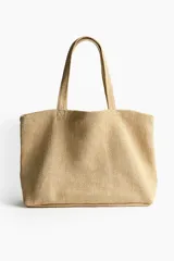 Bolso de playa tipo tote de tejido texturizado en color beige, con dos asas superiores para llevar al hombro.