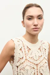 Top sin mangas confeccionado en tejido de crochet con patrón geométrico y floral, en color beige claro.