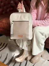 Mochila de cuero en color crudo, con bolsillo frontal con cierre y detalle de textura grabada. Cuenta con tiras ajustables y manija superior.
