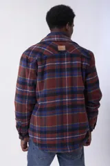 Sobrecamisa de corte holgado con diseño a cuadros en tonos beige y marrón, confeccionada en tejido de textura suave. Presenta cuello clásico, cierre frontal con botones, dos bolsillos con solapa en el pecho y puños abotonados.