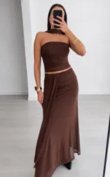 Conjunto de dos piezas marrón, compuesto por un top strapless fruncido con accesorio para el cuello y una pollera larga con drapeado frontal.