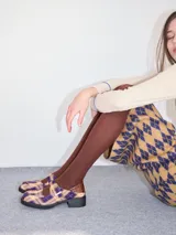 Zapatos tipo guillermina con punta cuadrada, confeccionados en lona resistente con estampado de cuadros escoceses en tonos beige, rojo y negro. Presentan una correa ajustable con hebilla metálica color bronce y una suela con taco de 4 cm.