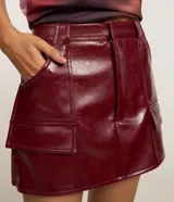 Short pollera de tiro medio confeccionado en poliuretano con acabado símil cuero. Presenta diseño de corte recto, cierre frontal con cremallera, trabillas para cinturón y dos bolsillos delanteros con solapa.