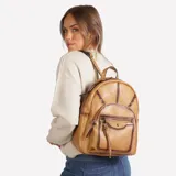 Mochila cartera Korium Vera de cuero sintético en color marrón, con diseño estructurado, bolsillo frontal con cierre y tachas decorativas en la parte superior.