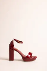 Sandalias de taco alto y plataforma, de cuero color rojo brillante con efecto charol. Cuenta con una tira delantera, taco ancho, y tira ajustable al tobillo con hebilla dorada.
