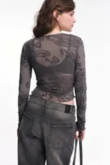 Remera rosa de manga larga, confeccionada en tela con transparencias y detalles en flock con estampado paisley. Tiene cuello a la base, corte al cuerpo y frunces laterales.