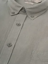 Camisa de manga larga color verde oliva, confeccionada en lino y poliéster, con cuello abotonado y bolsillo en el pecho con logo bordado.