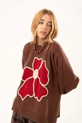 Buzo de punto color chocolate con diseño de flor grande en el frente en tonos rojos y centro texturizado en color crema. Presenta cuello redondo, mangas largas y puños y ruedo acanalados.