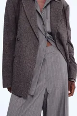 Pantalón sastrero de corte ancho y tiro alto, color gris oscuro con finas rayas verticales blancas (pinstripe). Presenta pliegues frontales (pinzas) y pretina con cierre oculto.