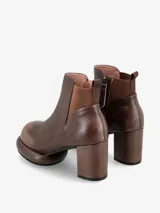 Bota corta tipo botineta de cuero negro con taco cuadrado y plataforma redondeada. Presenta un panel elástico lateral en color crema y tirador en la parte trasera.