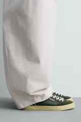 Zapatilla deportiva de estilo retro con diseño de paneles en cuero sintético color verde oscuro, detalles en crema y suela de goma en contraste.