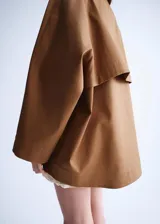 Chaqueta oversize color tostado con cuello embudo, manga larga, bolsillos laterales y bolsillos de parche con solapa. Cuenta con cierre delantero de cremallera y botones ocultos bajo tapeta, y forro interior.