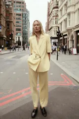 Blazer color amarillo pastel con textura, cuello solapa, manga corta con hombreras, bolsillos de vivo en delantero, forro interior y cierre frontal cruzado con botones.