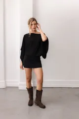 Blusa fluida de color marrón, con diseño holgado, escote bote que deja un hombro al descubierto y mangas anchas y cortas.