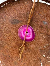 Collar con dije de piedra ágata blanca y marrón, con forma circular irregular y agujero en el centro. El dije está sujeto con un cordón fino de cuero marrón.