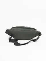 Riñonera de diseño urbano color verde militar, confeccionada en material resistente. Cuenta con dos compartimentos principales con cierre, correas laterales ajustables con hebillas y parche frontal con logo de la marca. Posee correa regulable con broche de seguridad para uso en cintura o cruzada.