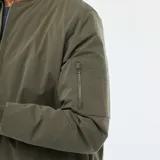 Campera estilo bomber color verde militar, con cierre frontal, cuello, puños y ruedo de tejido elástico acanalado. Presenta un bolsillo con cierre en la manga izquierda.
