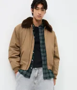 Campera bomber de sarga color tostado con cuello desmontable de pelo sintético oscuro. Presenta cierre frontal de cremallera, puños y cintura acanalados, y bolsillos laterales.