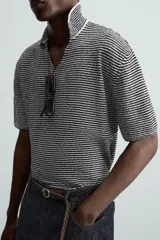 Polo de punto de manga corta con cuello solapa y abertura frontal en forma de V. Presenta un patrón de rayas horizontales finas en blanco y negro, con un acabado texturizado y un calce relajado.