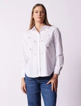 Camisa blanca de algodón con cuello clásico, escote en V y cierre frontal con botones. Presenta apliques de brillos plateados en el frente y mangas largas con puños abotonados.