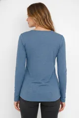 Remera blanca de manga larga, entallada, con cuello redondo y una hilera de botones en el frente. Incluye un pequeño bolsillo decorativo en el pecho.