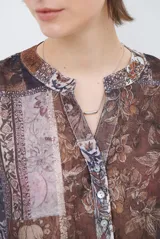Camisa de corte recto con cuello mao y cierre frontal parcial de botones. Presenta un diseño estampado tipo patchwork con motivos florales y geométricos en tonos tierra, marrones y beige. Posee mangas tres cuartos con puños simples.