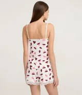 Conjunto de pijama estilo short doll compuesto por una blusa con breteles finos ajustables, escote en V con detalle de encaje, y un short corto con cintura elástica y borde de encaje. Ambas piezas presentan un estampado de corazones en tonos rosados y morados sobre fondo blanco.