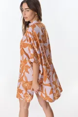 Camisa larga de lino con estampado floral azul sobre fondo beige. Posee cuello mao, mangas cortas con puños, botones metálicos a la vista y tajos laterales en el ruedo.