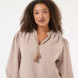 Blusa de corte fluido con estampado de cuadros vichy en tonos beige y blanco. Presenta cuello mao con cordón ajustable terminado en borlas y mangas largas abullonadas con puños elásticos.