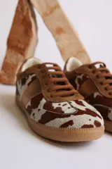 Zapatillas deportivas con estampado animal print de vaca en blanco y negro, con detalles en cuero sintético plateado en los laterales y talón.