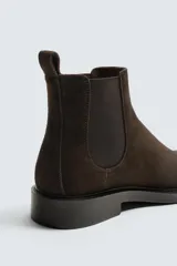 Bota estilo Chelsea con parte superior de piel con acabado en serraje, elásticos laterales para facilitar el calce, horma redonda y suela con ligero tacón.