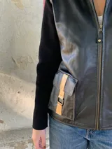 Campera negra de cuero con mangas largas de lana y bolsillos frontales con detalles dorados.