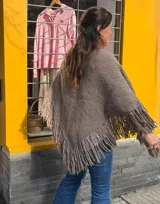 Ruana triangular de lana merino color marrón, con diseño tejido de punto y flecos en el borde inferior.