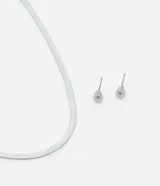 Conjunto de joyería compuesto por un collar tipo cinta italiana y un par de aros tipo caravana con diseño de gota y detalle de cristal. Fabricado en metal con acabado plateado.
