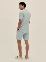 Conjunto de camisa de manga corta con cuello solapa y short con cordón ajustable, ambos en tejido ligero a rayas verticales celestes y blancas.