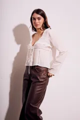 Blusa blanca de algodón con escote en V, mangas largas con detalles de encaje y cierre frontal con lazos.