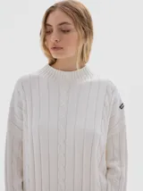 Buzo tejido de punto color beige, con cuello subido, diseño oversized y aberturas laterales en el ruedo.