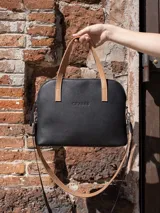 Cartera negra de cuero genuino con correa corta de cuero color tostado y correa larga de cinta negra con letras blancas.